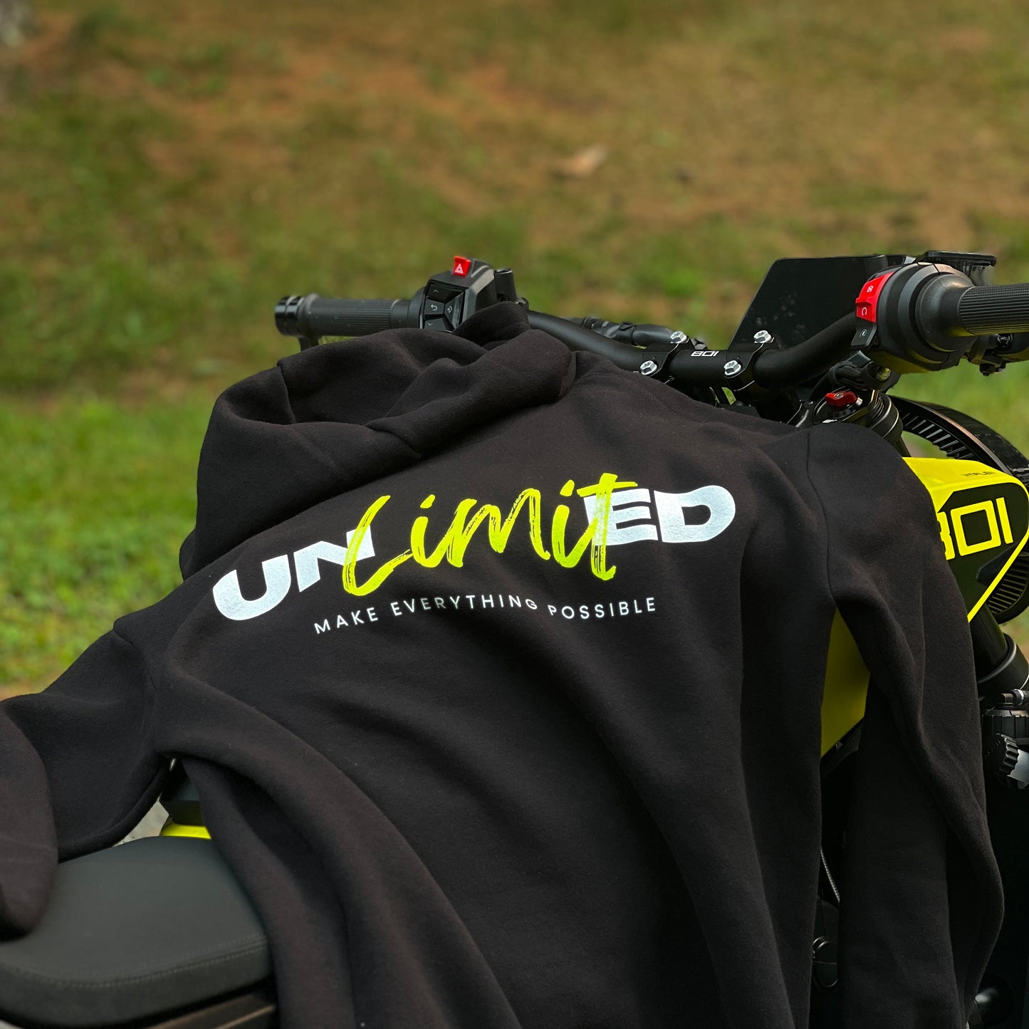 Black hoodie with 'UNLIMITED' logo on a motorcycle in a grassy area